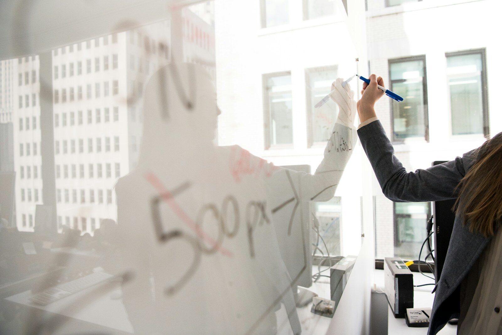 Person mapping out ideas on a glass office whiteboard